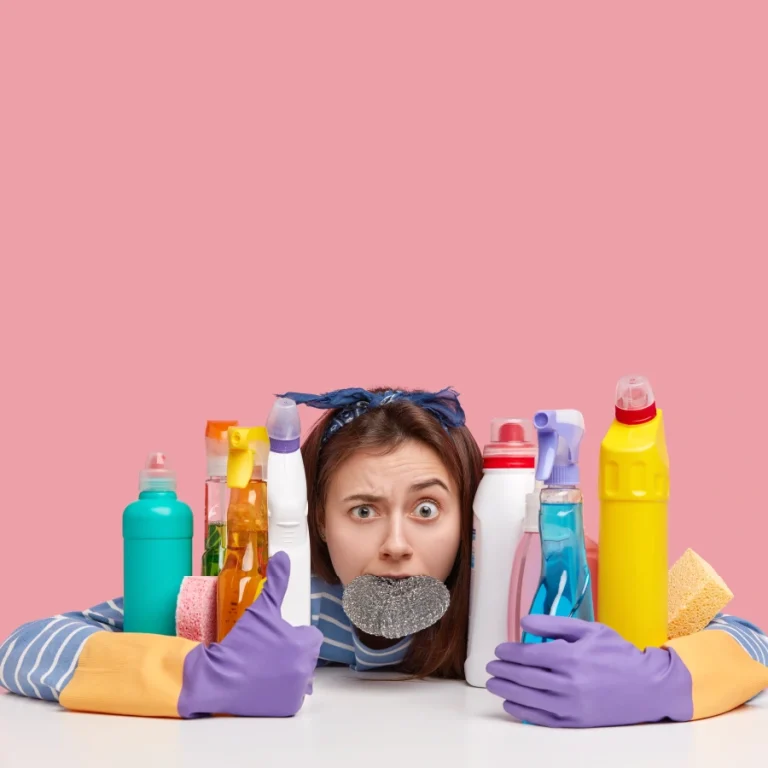 Una chica abrazando muchos productos de limpieza de tapicería con cara de asombro, sobre fondo Rosa